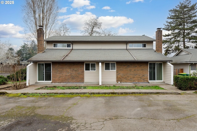 back of house with brick siding, a chimney, and fence