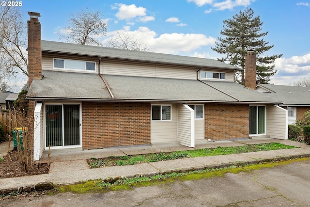 back of property featuring brick siding, a chimney, and a shingled roof