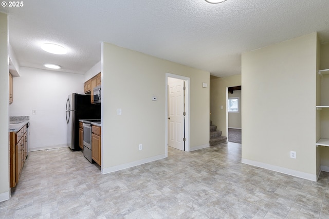 kitchen featuring baseboards, brown cabinets, a textured ceiling, and appliances with stainless steel finishes
