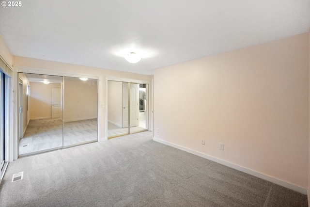 unfurnished bedroom with two closets and light colored carpet