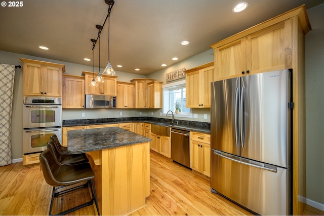 kitchen featuring recessed lighting, appliances with stainless steel finishes, a sink, a kitchen island, and light wood-type flooring