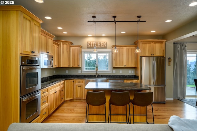 kitchen with dark countertops, light wood-style floors, appliances with stainless steel finishes, and a sink