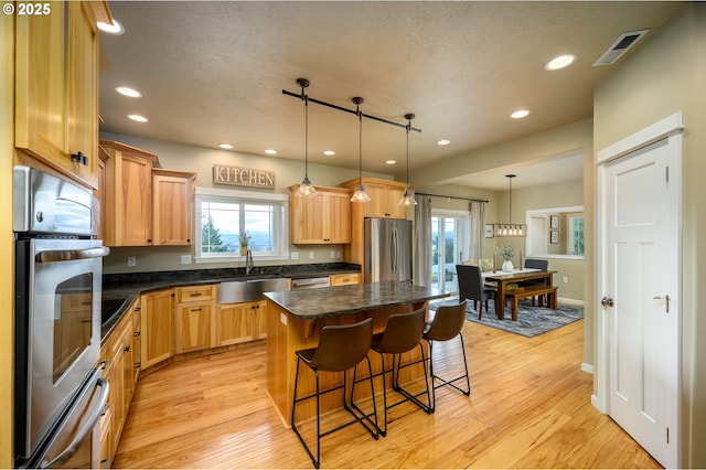 kitchen featuring a kitchen island, a sink, visible vents, light wood-style floors, and appliances with stainless steel finishes