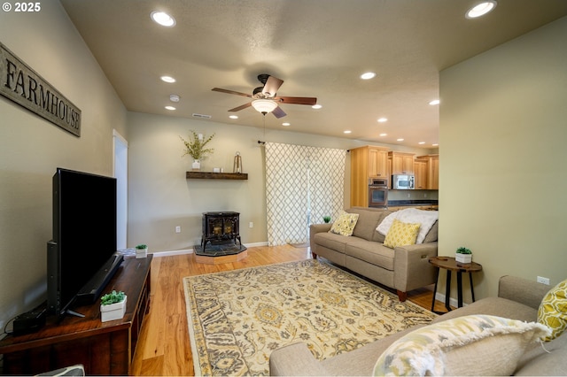 living area featuring light wood finished floors, recessed lighting, a ceiling fan, a wood stove, and baseboards