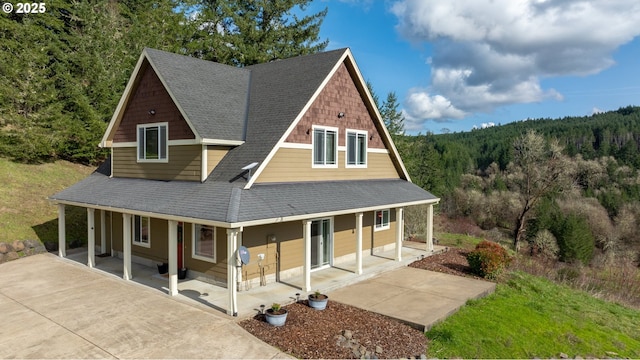 farmhouse with a porch, a view of trees, and roof with shingles