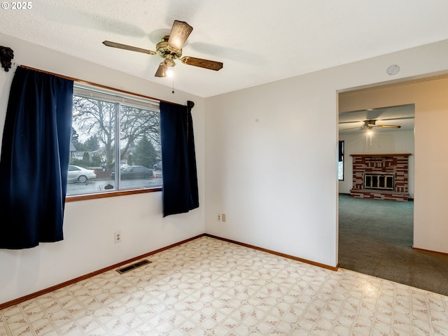 empty room with a fireplace, a ceiling fan, baseboards, visible vents, and tile patterned floors