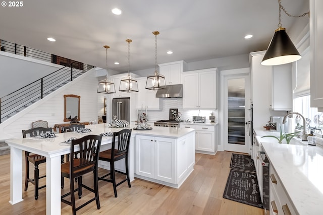 kitchen featuring white cabinets, a kitchen island, decorative light fixtures, high end fridge, and stove