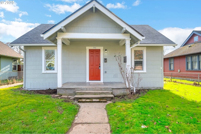 bungalow-style home featuring a porch, roof with shingles, a front lawn, and fence