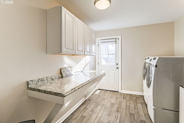 clothes washing area with light hardwood / wood-style floors, cabinets, and washing machine and clothes dryer