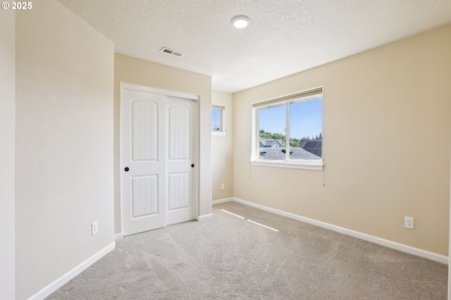 unfurnished bedroom with carpet flooring, a textured ceiling, baseboards, visible vents, and a closet
