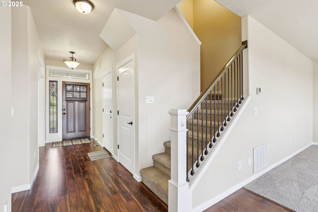 entryway featuring a textured ceiling, visible vents, wood finished floors, stairway, and baseboards