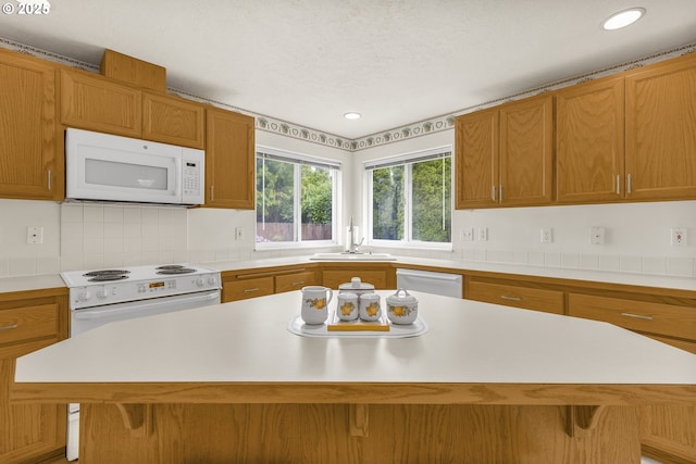 kitchen with white appliances, a sink, light countertops, a kitchen island, and a kitchen bar
