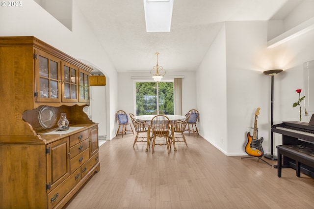 dining room featuring light wood-style floors, lofted ceiling, baseboards, and arched walkways