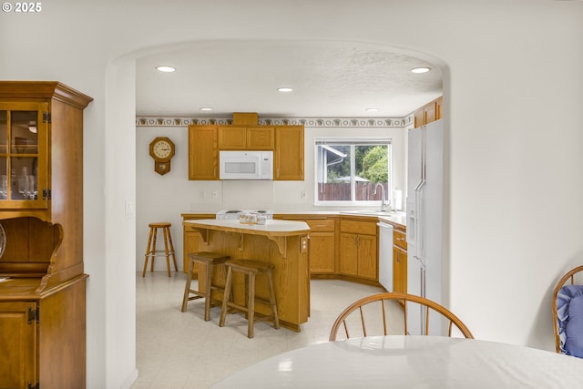kitchen with white appliances, a sink, a breakfast bar area, light countertops, and a kitchen island