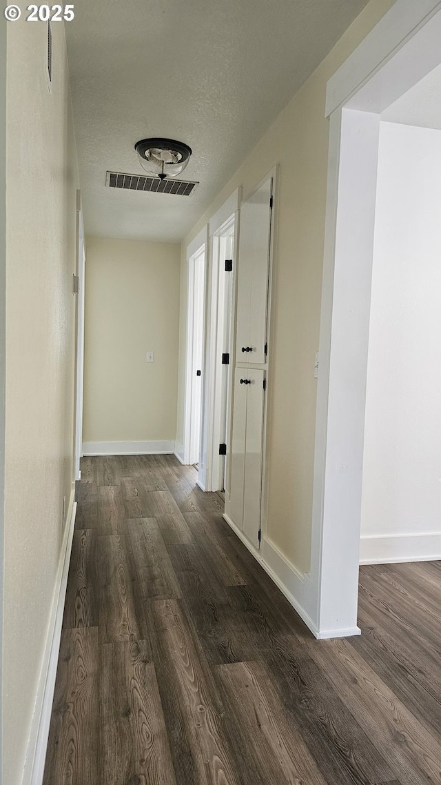 corridor with baseboards, visible vents, dark wood finished floors, and a textured ceiling