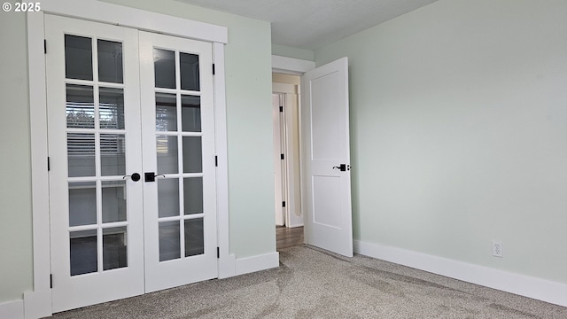 carpeted spare room featuring french doors and baseboards