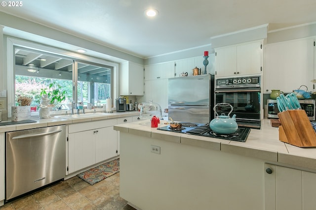 kitchen with stone finish flooring, a sink, tile counters, white cabinets, and black appliances