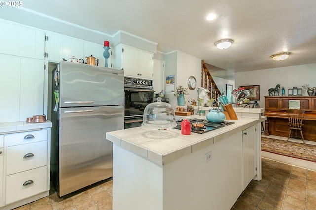 kitchen with white cabinets, tile countertops, a textured ceiling, appliances with stainless steel finishes, and a kitchen island