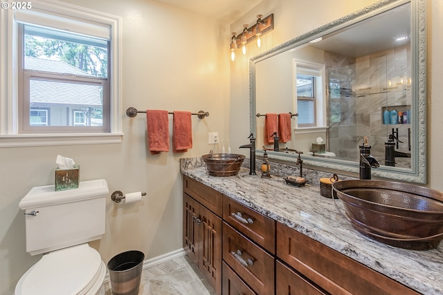 bathroom featuring a sink, toilet, baseboards, and tiled shower