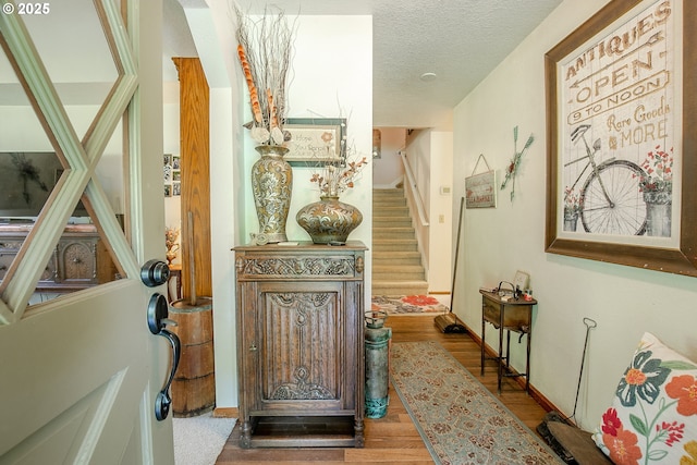 corridor with a textured ceiling, wood finished floors, baseboards, and stairs