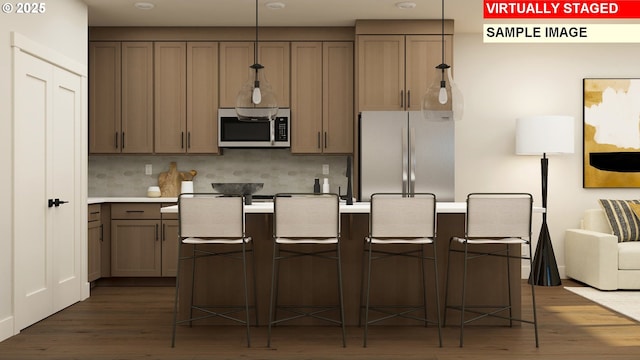 kitchen featuring dark wood-type flooring, a center island with sink, light countertops, tasteful backsplash, and appliances with stainless steel finishes
