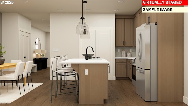 kitchen featuring freestanding refrigerator, a sink, dark wood-type flooring, light countertops, and an island with sink
