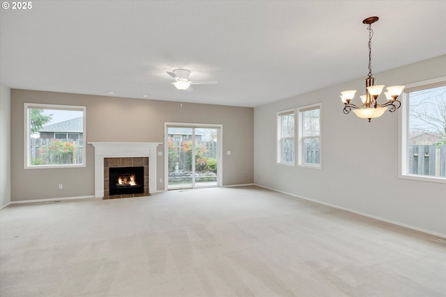 unfurnished living room featuring ceiling fan with notable chandelier, a tile fireplace, and light carpet