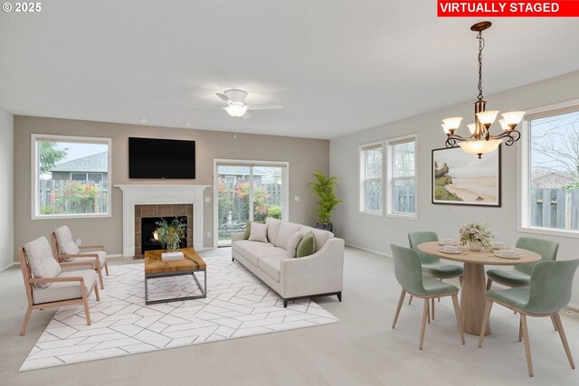 carpeted living room with a tiled fireplace and ceiling fan with notable chandelier