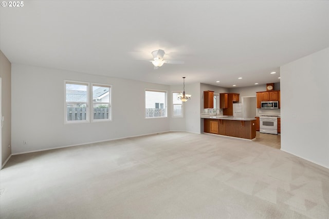 unfurnished living room with ceiling fan with notable chandelier, sink, and light colored carpet