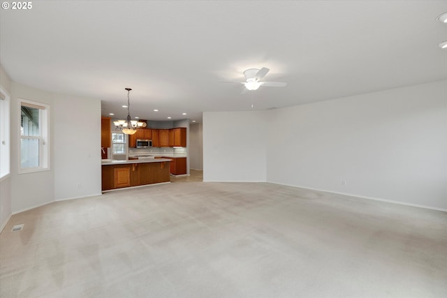 unfurnished living room featuring ceiling fan with notable chandelier and light colored carpet