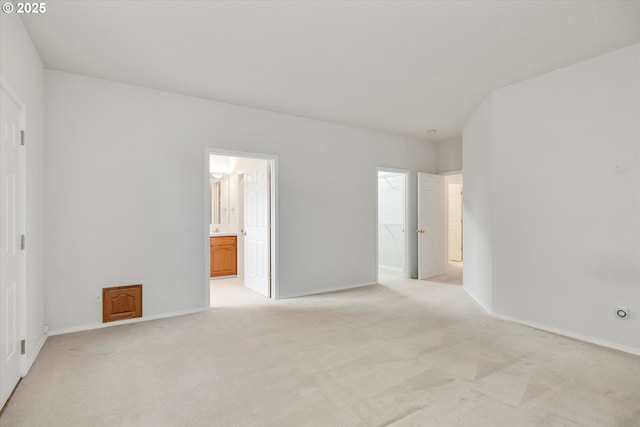 unfurnished bedroom featuring a closet, ensuite bathroom, a spacious closet, and light carpet