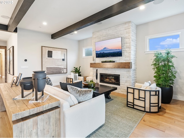 living room featuring beam ceiling, a stone fireplace, a wealth of natural light, and hardwood / wood-style flooring