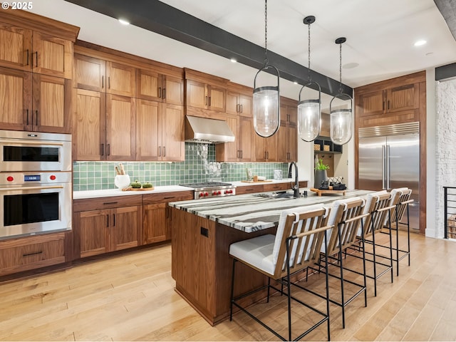 kitchen with pendant lighting, a center island with sink, stainless steel appliances, a kitchen bar, and wall chimney exhaust hood