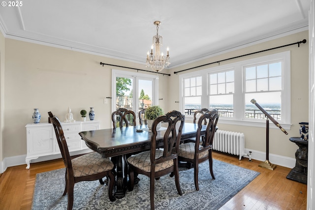 dining room featuring a chandelier, baseboards, light wood-type flooring, radiator, and crown molding