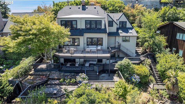 back of house with a shingled roof, stairway, a wooden deck, stucco siding, and a chimney