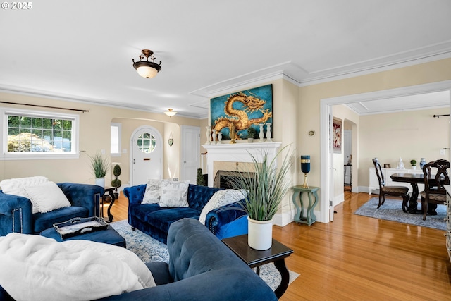 living room with arched walkways, light wood finished floors, a fireplace, and crown molding