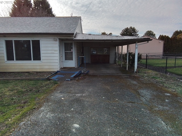 view of front of house with driveway, fence, a carport, and roof with shingles