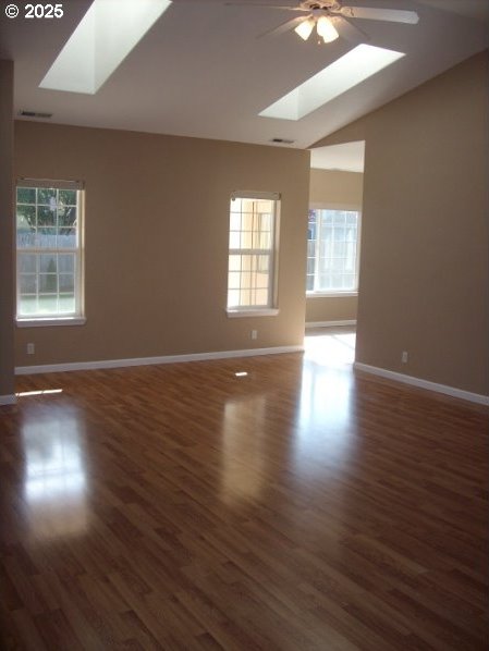 unfurnished room featuring vaulted ceiling with skylight, dark hardwood / wood-style floors, and ceiling fan