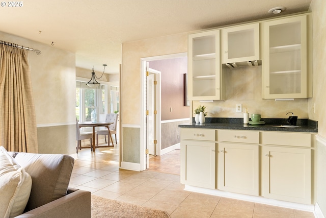 kitchen featuring a sink, light tile patterned flooring, dark countertops, glass insert cabinets, and baseboards