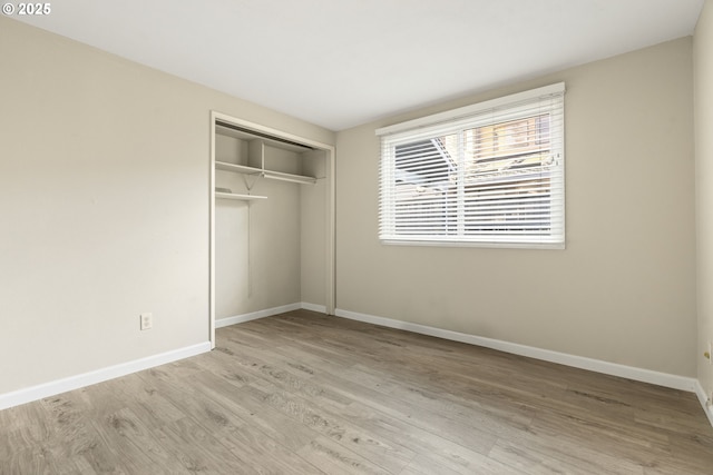 unfurnished bedroom with wood finished floors, baseboards, and a closet