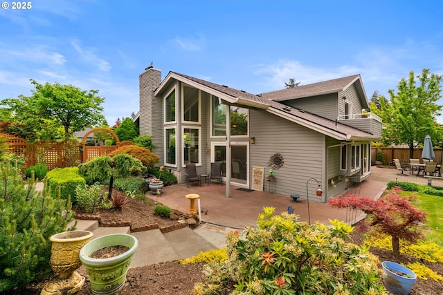 rear view of house featuring fence, a patio area, a chimney, a wooden deck, and roof with shingles