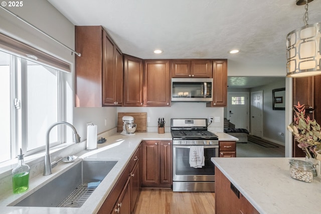 kitchen with light wood-type flooring, hanging light fixtures, brown cabinetry, stainless steel appliances, and a sink