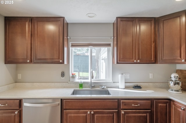 kitchen featuring stainless steel dishwasher, light countertops, brown cabinets, and a sink