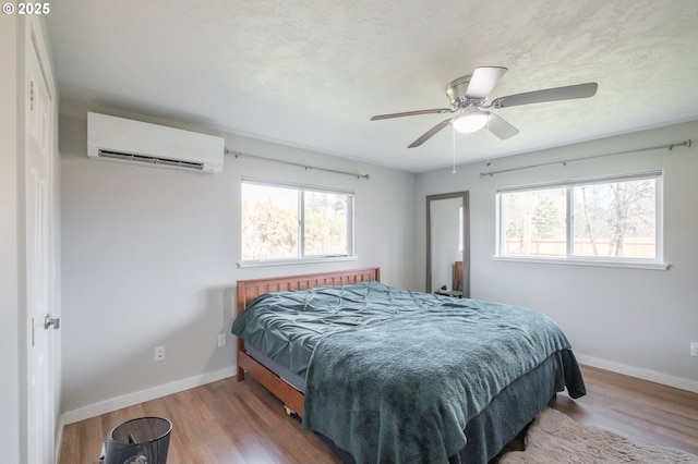 bedroom with wood finished floors, baseboards, and a wall mounted AC