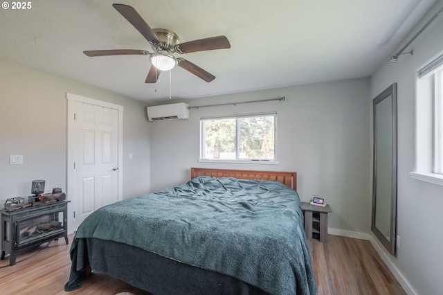 bedroom with a wall mounted air conditioner, a ceiling fan, baseboards, and wood finished floors