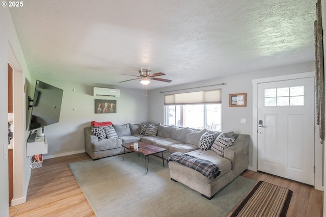 living room featuring an AC wall unit, a ceiling fan, a textured ceiling, light wood-style floors, and baseboards