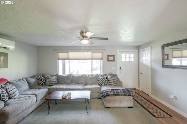 living room with a wealth of natural light, a wall mounted AC, baseboards, and wood finished floors