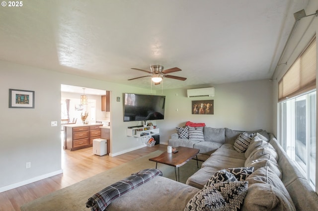 living area with baseboards, an AC wall unit, a ceiling fan, and light wood finished floors