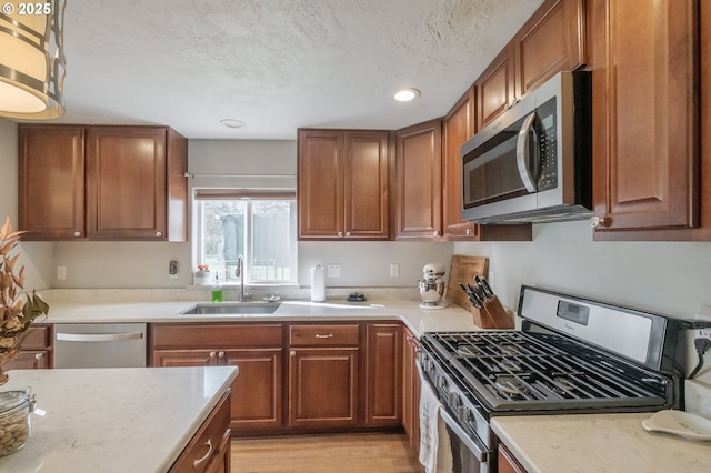 kitchen featuring a sink, stainless steel appliances, light wood-style floors, a textured ceiling, and brown cabinets