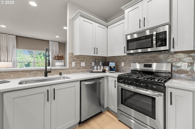 kitchen featuring light stone counters, a sink, white cabinetry, appliances with stainless steel finishes, and decorative backsplash